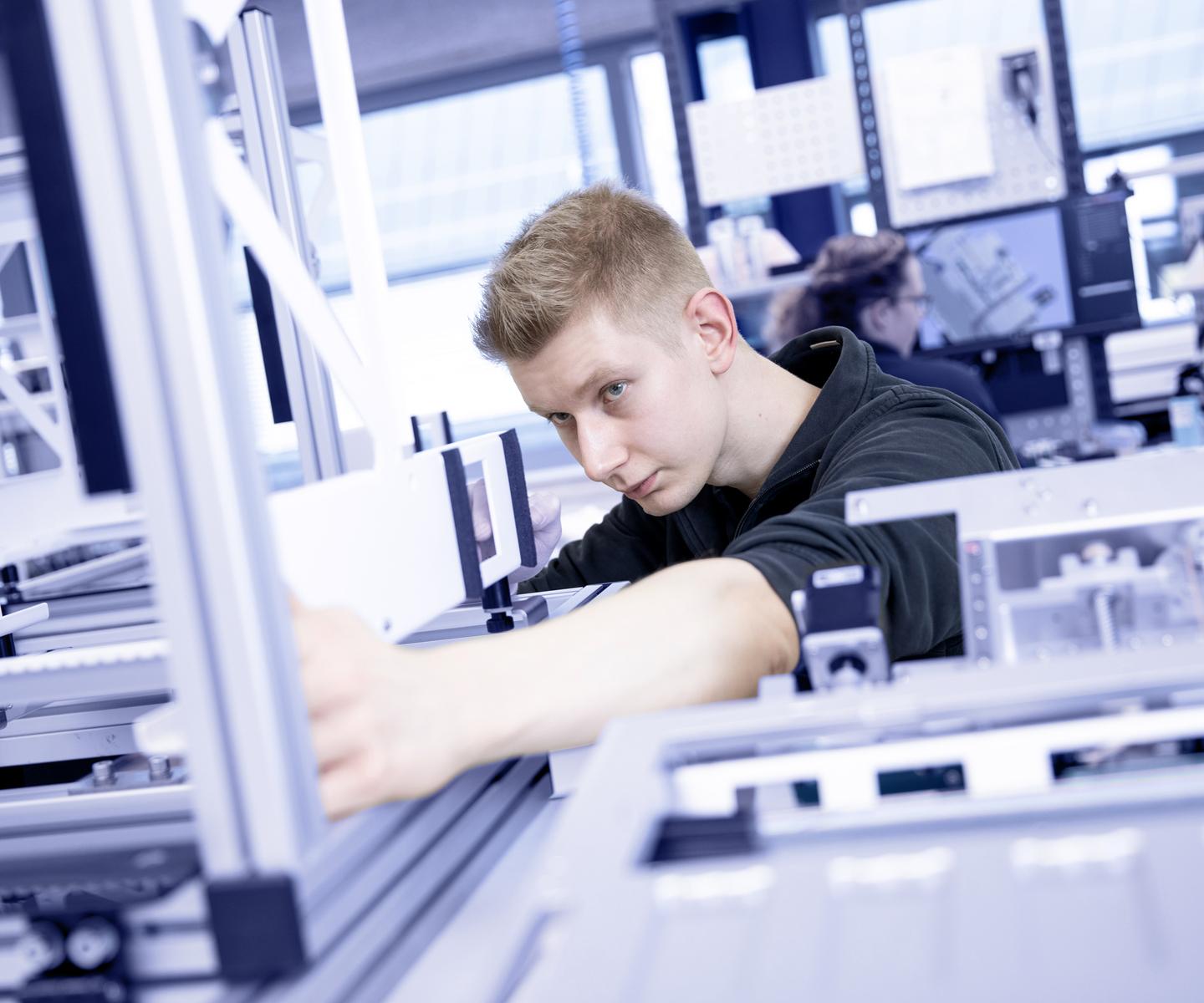 Ein junger Mann arbeitet konzentriert an einer technischen Vorrichtung in einer modernen Arbeitsumgebung.