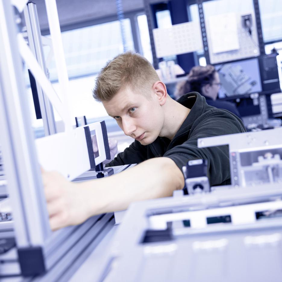 Ein junger Mann arbeitet konzentriert an einer technischen Vorrichtung in einer modernen Arbeitsumgebung.