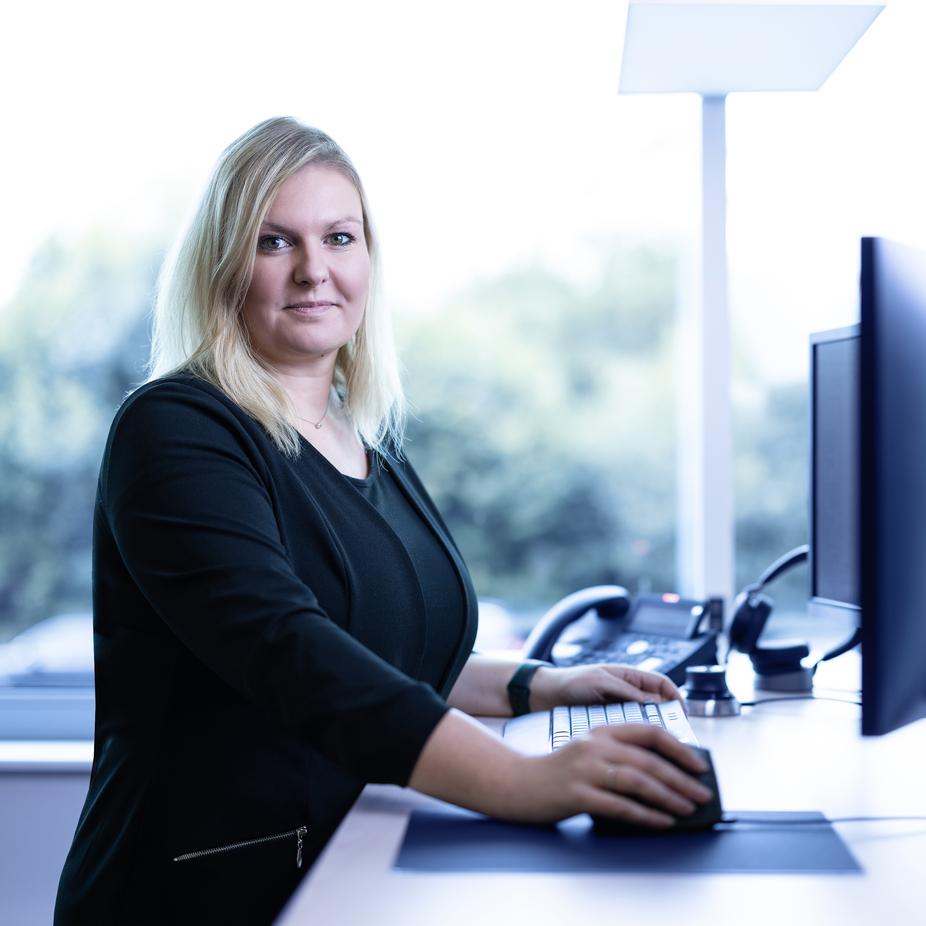 Frau mit blonden Haaren arbeitet an einem Computer an einem modernen Schreibtisch mit Blick aus einem Fenster.