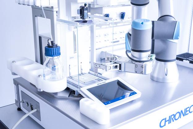 Nahaufnahme eines Labormessgeräts mit einer Pipette, einem Bildschirm und einer Flasche auf einem Tisch.