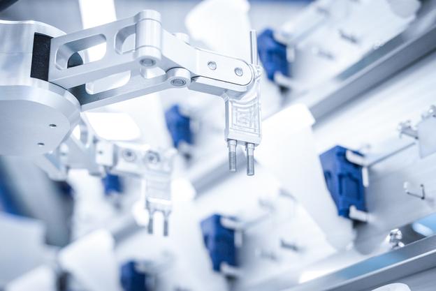 Nahaufnahme eines Industrieroboterarms mit Greifer und mehreren blauen Bauteilen im Hintergrund.