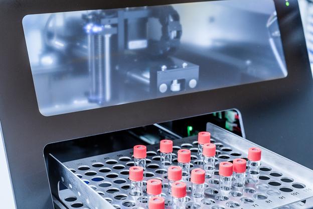 Nahaufnahme einer Laborapparatur mit einem Behälter für Glasfläschchen mit roten Verschlüssen.