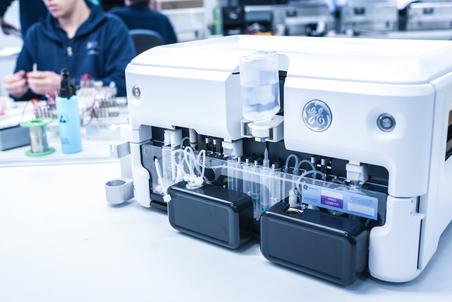 Detail view of an analytical device with tubing and containers in a lab.