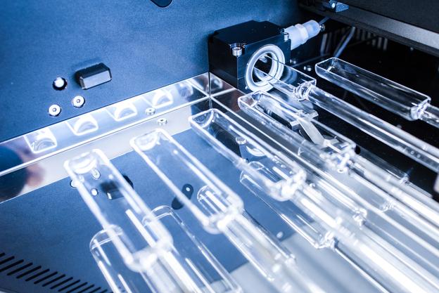 Nahaufnahme von transparenten Glaskolben in einem technischen Gerät mit Steuerungselementen im Hintergrund.