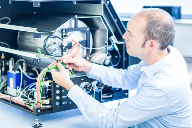 Mann arbeitet an der Verkabelung eines technischen Geräts in einem hellen, modernen Arbeitsumfeld.