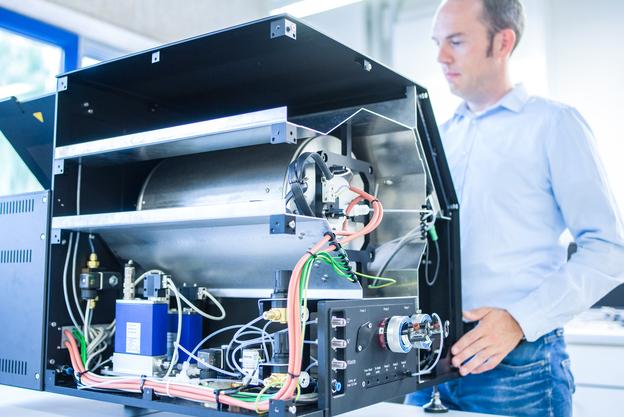 Mann untersucht das Innere einer technischen Apparatur mit sichtbaren Schl&auml;uchen und Ger&auml;ten in einem modernen Umfeld.