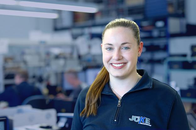 eine junge Elektronikerin steht in der Montage von Ger&auml;ten und schaut l&auml;chelnd in die Kamera